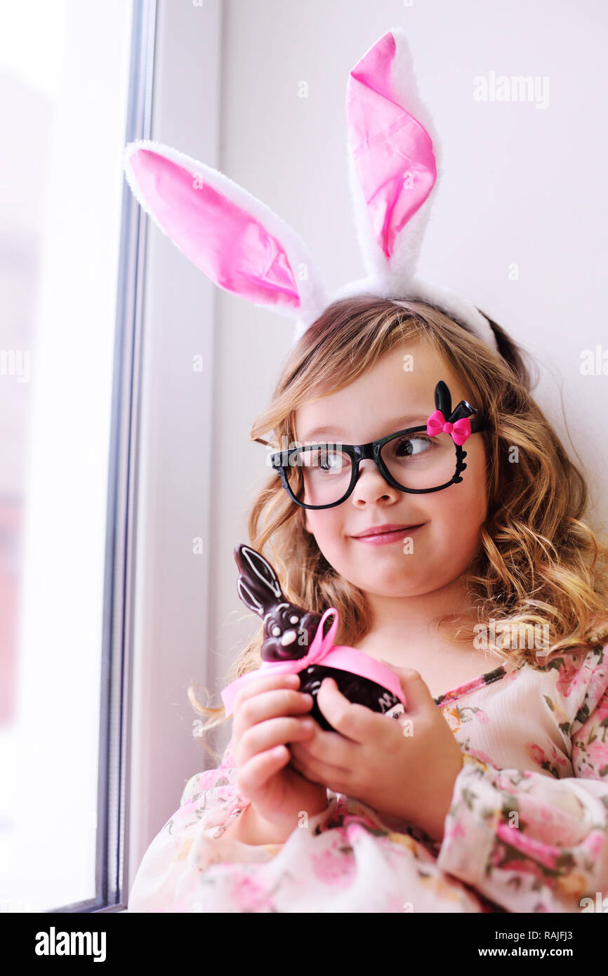 Bebe Nina Bonita En Un Elegante Vestido Con Orejas De Conejo En Su Cabeza Sosteniendo Un Conejito De Pascua De Chocolate Fotografia De Stock Alamy