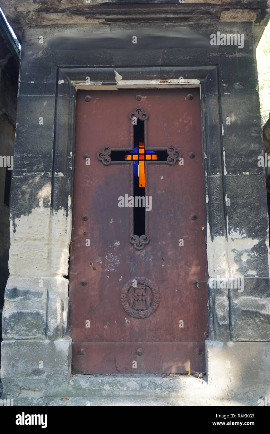 Lápida antigua de piedra con una puerta de metal oxidado y vidrio manchado cruz en la espalda Foto de stock