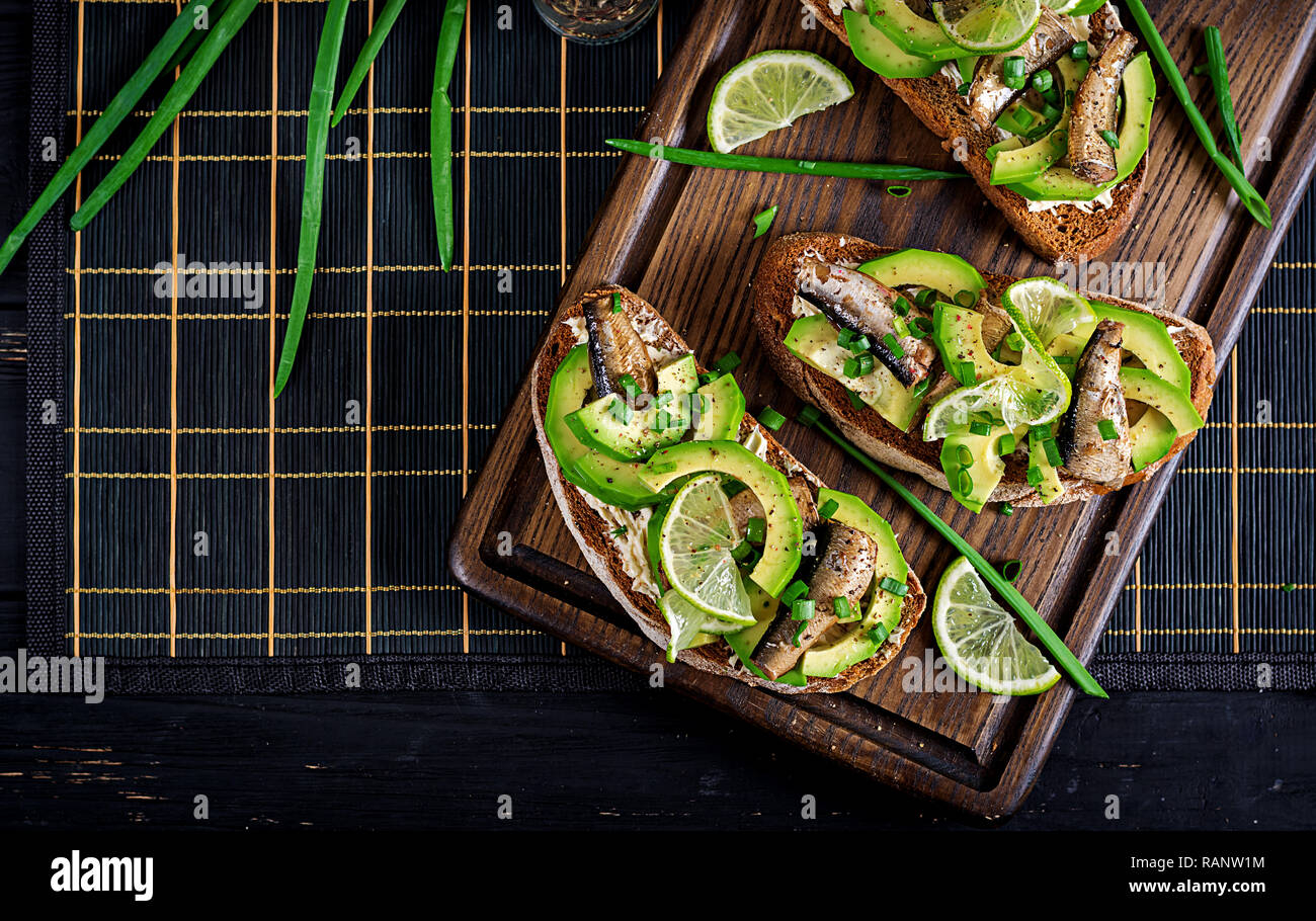 - Smorrebrod Sandwich con espadín, aguacate y queso crema sobre la plancha de madera. Cocina danesa. Vista superior Foto de stock