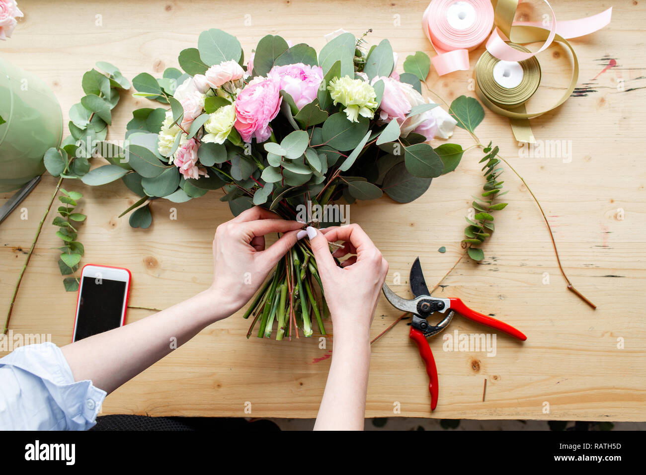 Close-up de mano florist profesional haciendo un ramo de rosas ranúnculos y  peonías en una tienda de flores. Disposición y embalaje del ramo. El  concepto de entrega de flores y tienda online