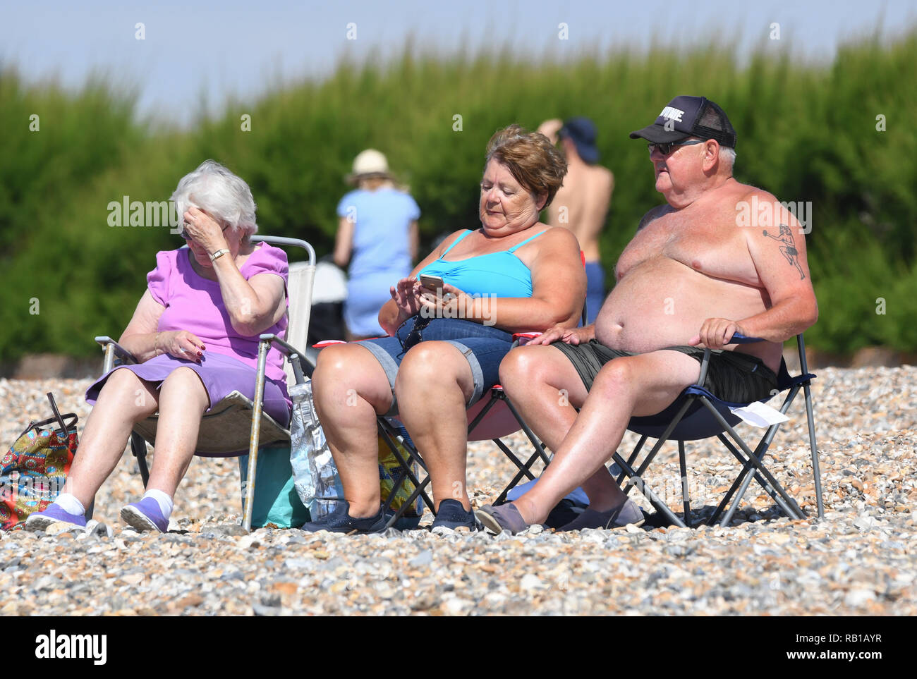 Grupo de gente sentada al sol en la playa en un día caluroso en el verano de 2018 ola de calor en el Reino Unido. Foto de stock