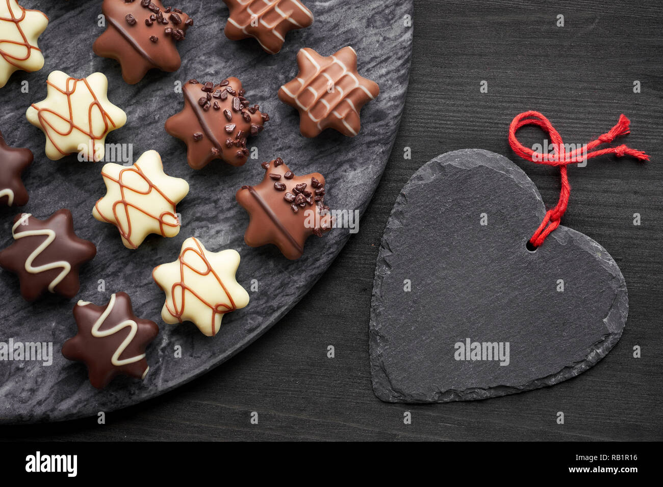 Chocolates en forma de estrella en la placa de piedra gris oscura con corazón negro sobre fondo de textura oscura Foto de stock