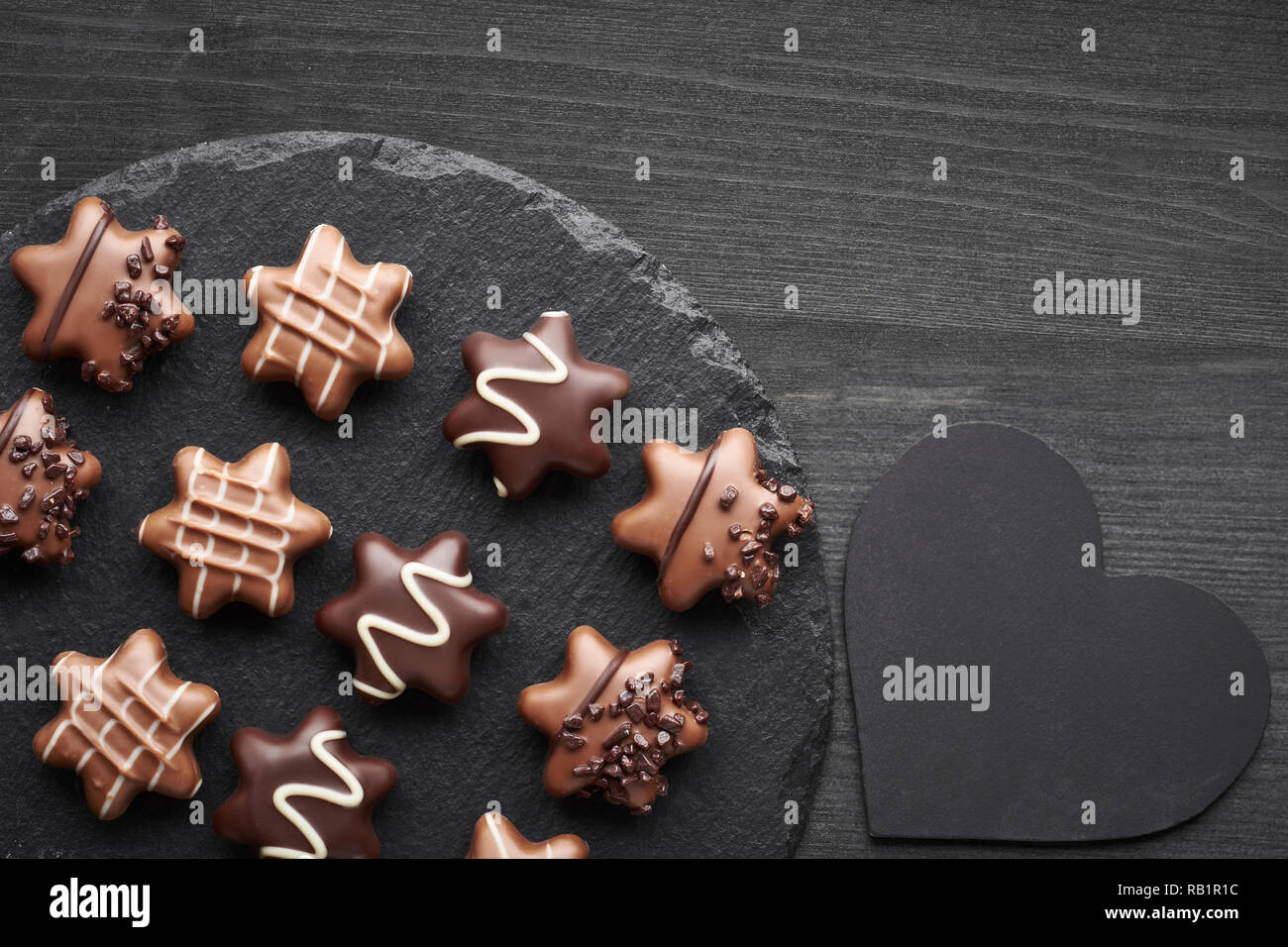 Chocolates en forma de estrella en el oscuro fondo de textura con corazón negro Foto de stock