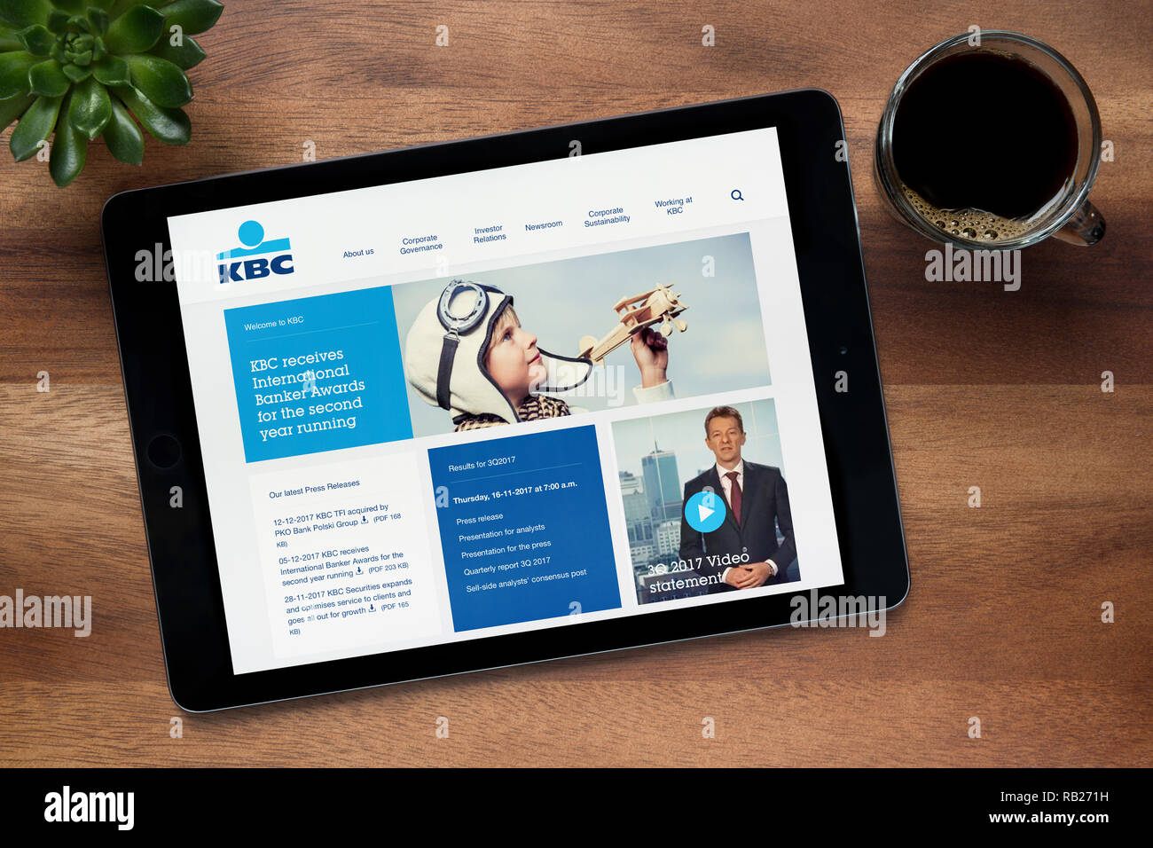 El sitio web de KBC Bank es visto en un iPad, en una mesa de madera junto con un café espresso y una planta de casa (Editorial). Foto de stock