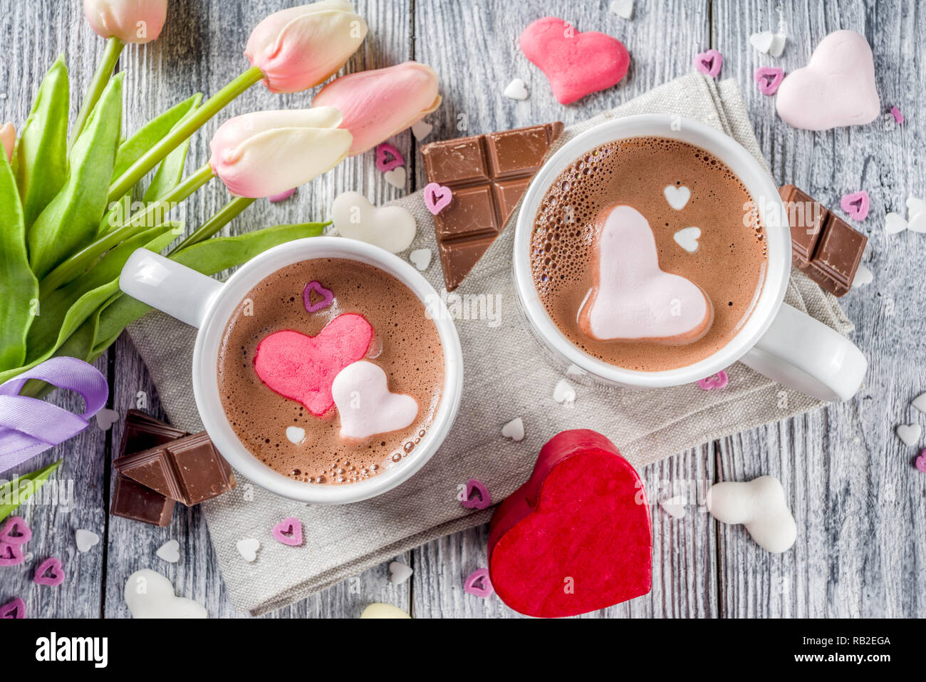 Día de San Valentín tratar ideas, dos tazas de bebida de chocolate caliente con malvavisco corazones rojo color blanco rosado con trozos de chocolate, espolvorea azúcar, madera vieja Foto de stock