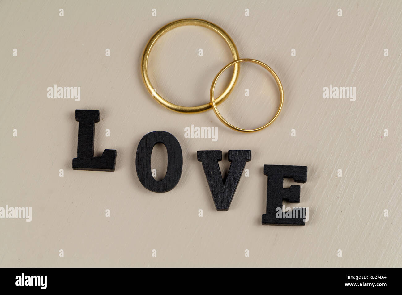 Dos anillos de boda hechas en oro y la palabra amor en letra negra Foto de stock