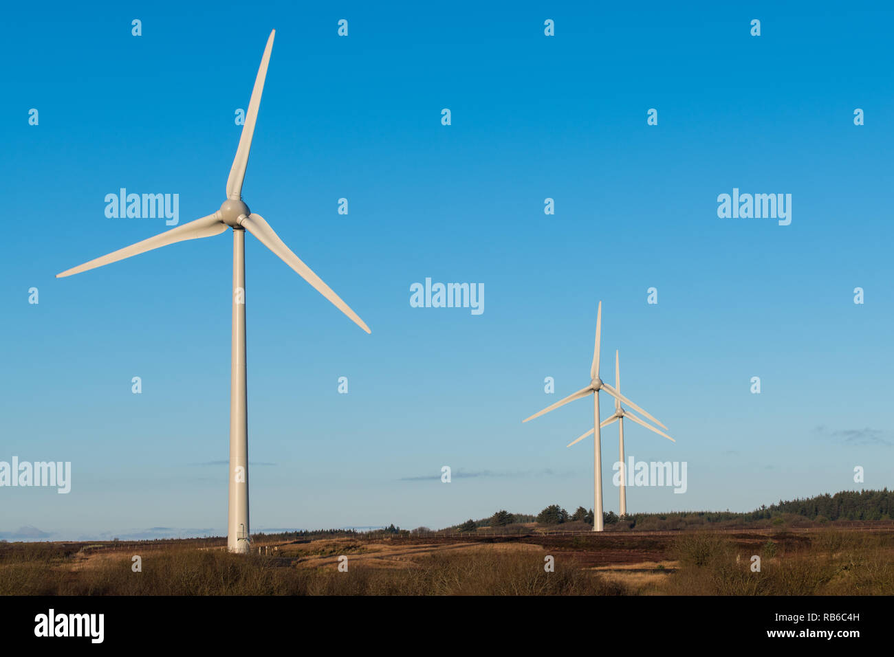 Una escena de las energías renovables y la energía verde con un grupo de tres molinos de viento bajo un hermoso cielo azul en Irlanda del Norte Foto de stock