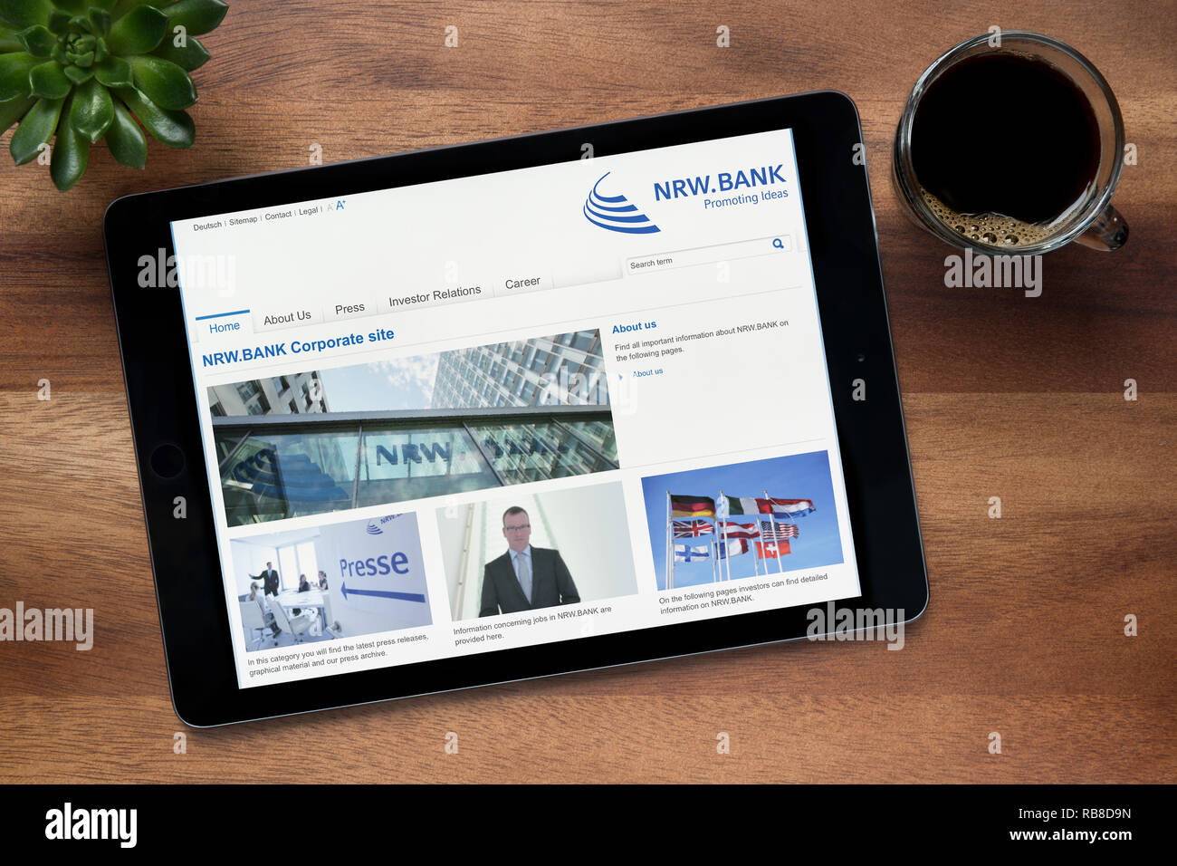 El sitio web de NRW Banco es visto en un iPad, en una mesa de madera junto con un café espresso y una planta de casa (Editorial). Foto de stock