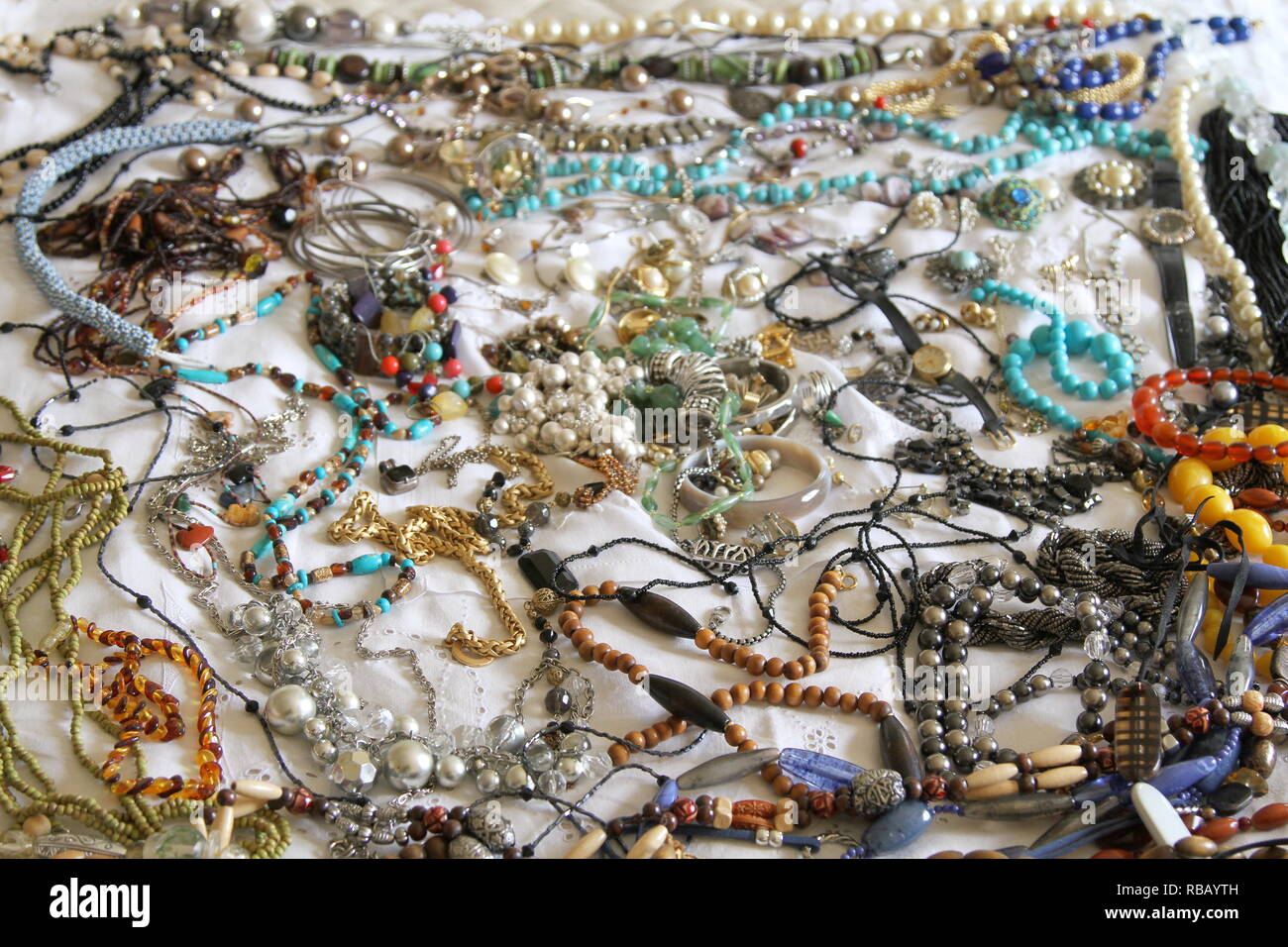 Joyería. Una colección de joyas, sentado sobre una cama con una sábana blanca. Joyas. Los objetos de valor. La propiedad personal. Valor sentimental. Las piedras. Las perlas. Cordones. Collares. Pulseras. Un reloj de muñeca. Multicolor. Surtido. Foto de stock
