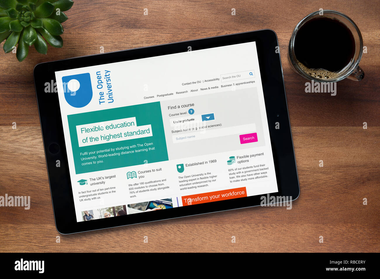 El sitio web de la Universidad Abierta es visto en un iPad, en una mesa de madera junto con un café espresso y una planta de casa (Editorial). Foto de stock