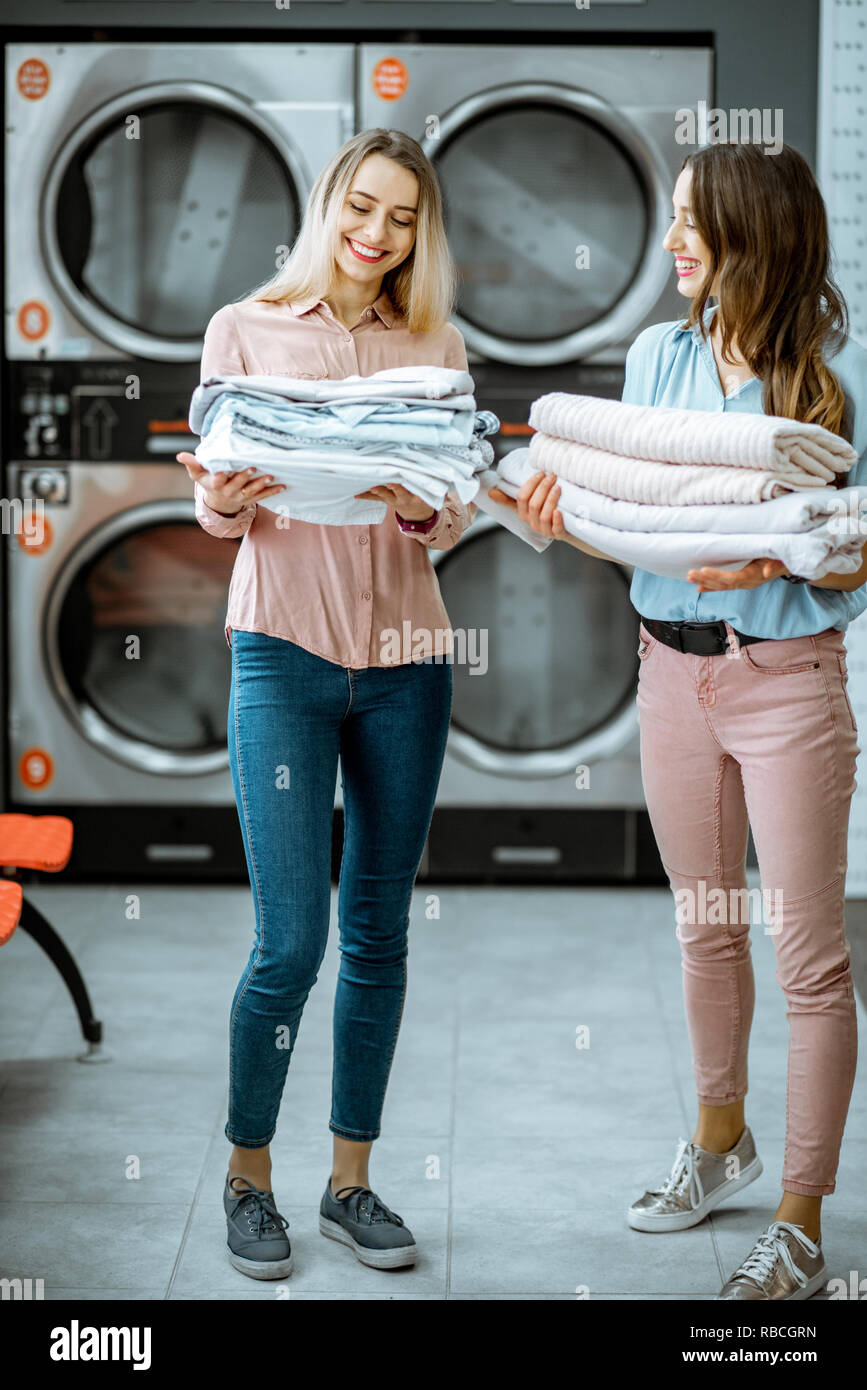 Dos jóvenes mujeres pie junto con ropa limpia en el auto servicio lavandería con en el fondo Fotografía de stock - Alamy