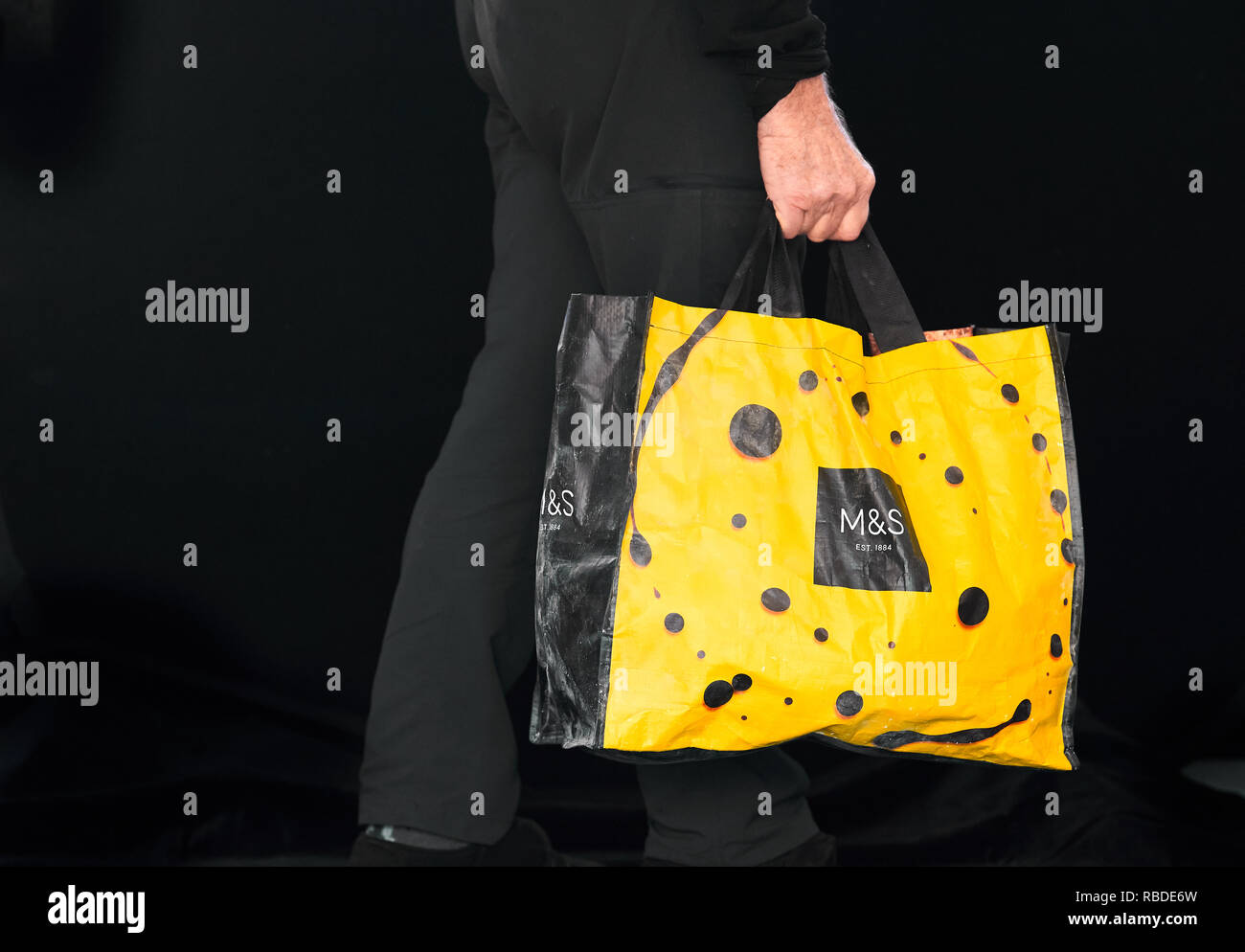 El hombre lleva una bolsa de compras reutilizable con comestibles después de salir de un M&S (Marks & Spencer) store. Foto de stock
