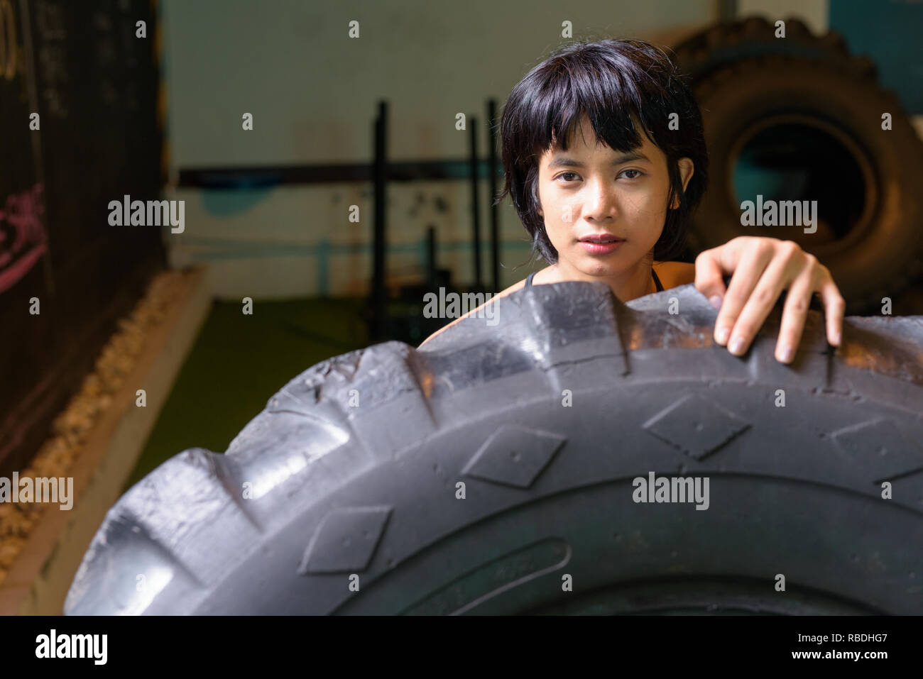 Asia mujer fitness empujando y voltear la carretilla rueda de neumático en el gimnasio Foto de stock