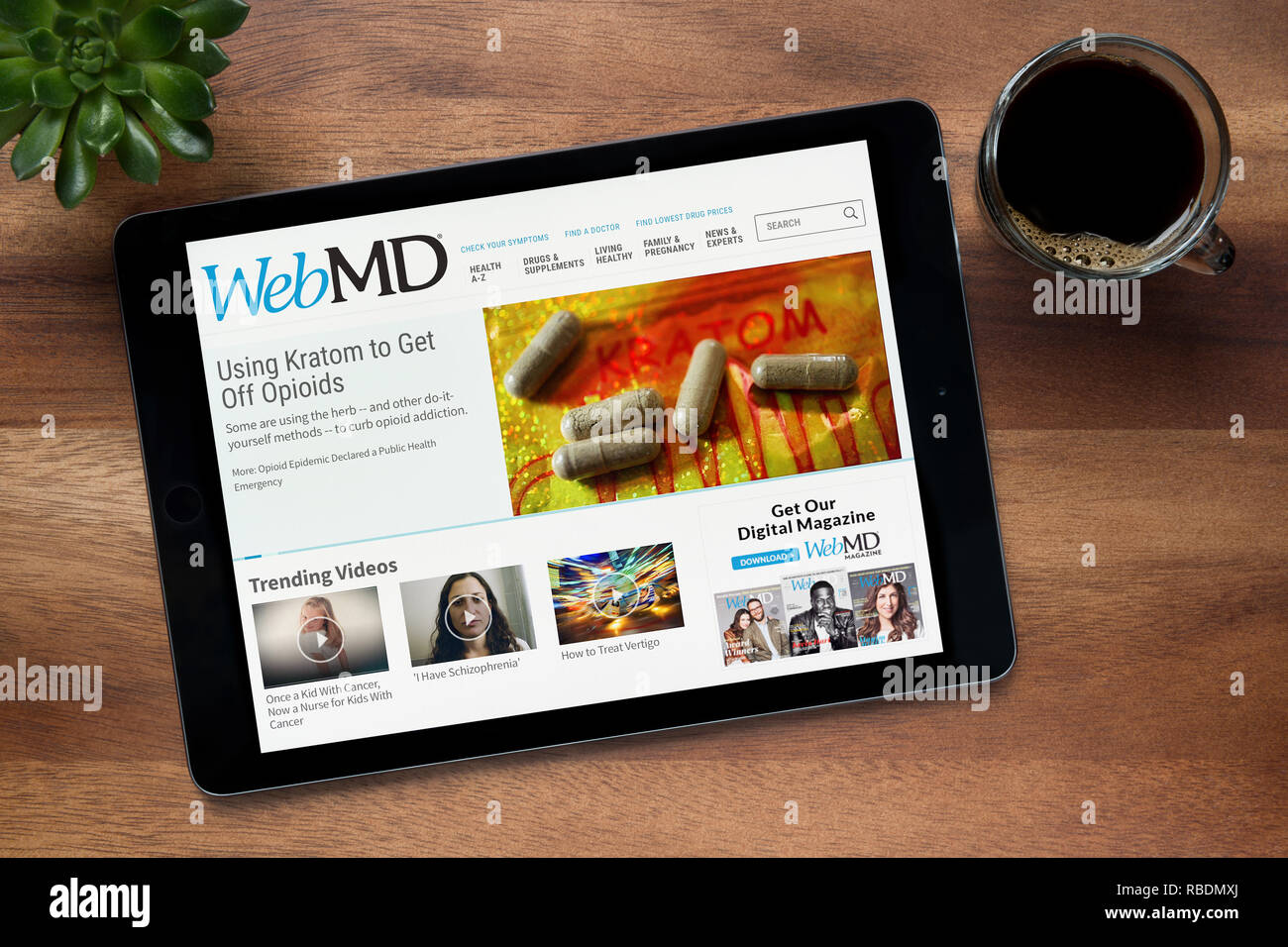 El sitio web de WebMD es visto en un iPad, en una mesa de madera junto con un café espresso y una planta de casa (Editorial). Foto de stock