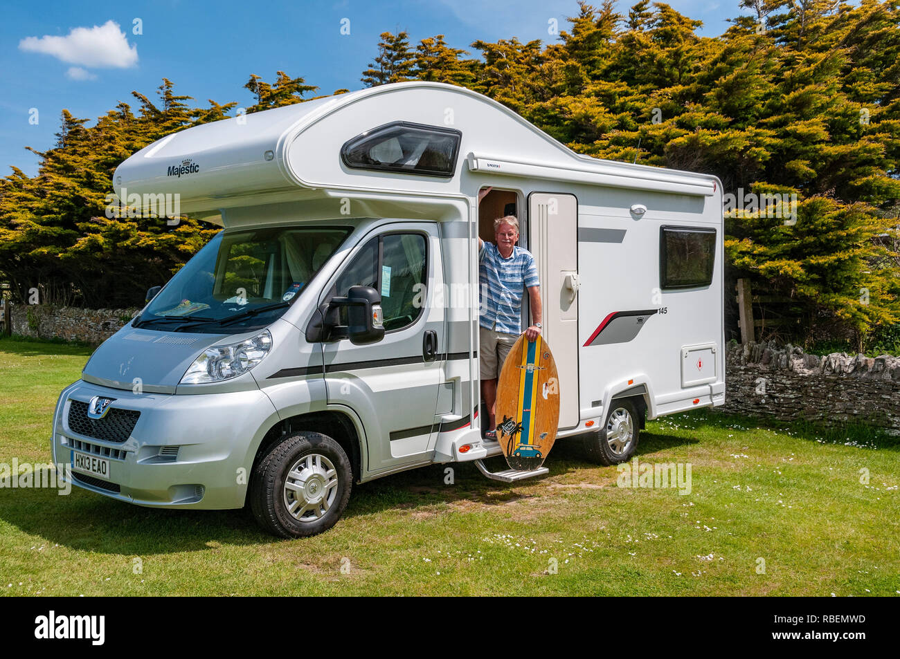 Hombre de pie con vacaciones skimboard en portada de autocaravana en día soleado en Croyde, Devon, Inglaterra, Reino Unido. Foto de stock