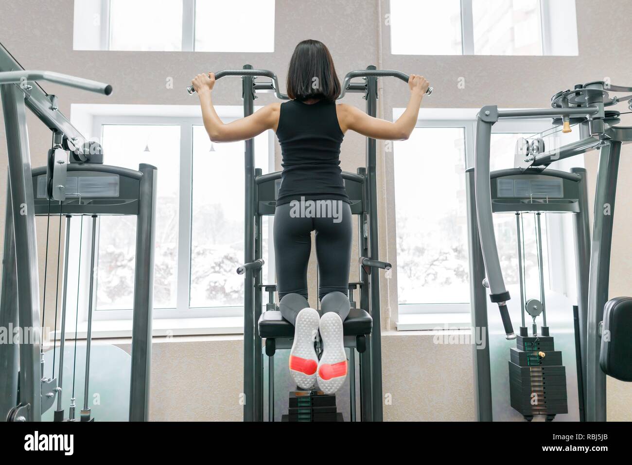Mujer joven haciendo ejercicios para la espalda en una máquina de fitness  en el gimnasio, vista desde la parte de atrás. Gimnasio, el deporte, la  formación, el concepto de pueblo Fotografía de