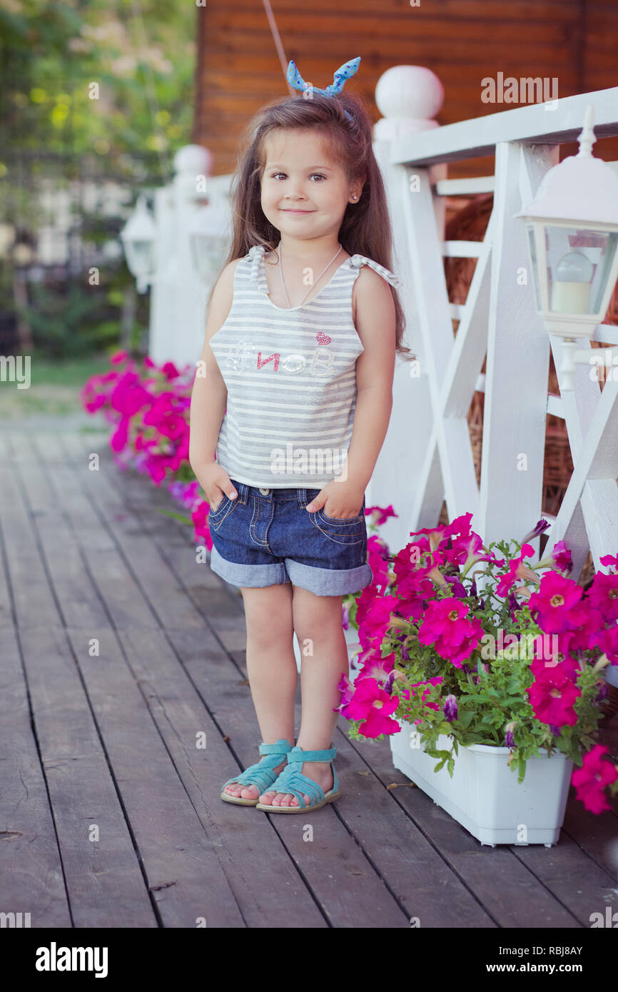 Elegante Hermoso Lindo Bebe Nina Morena Con Cabello Posando En El Jardin Lleno De Flores De Madera Vistiendo Camisetas Y Pantalones Vaqueros Diminutos Skivy Underwaist Aireado Y B Fotografia De Stock Alamy