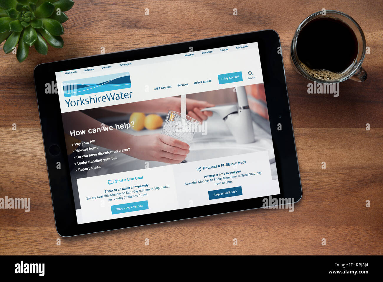 El sitio web de Yorkshire Water es visto en un iPad, en una mesa de madera junto con un café espresso y una planta de casa (Editorial). Foto de stock