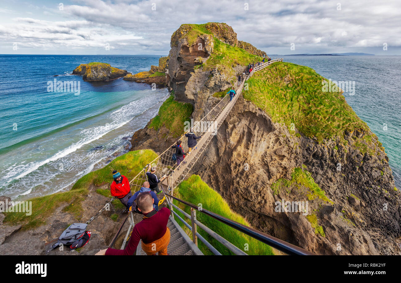 Turistas y visitantes explorar y cruzar el puente de cuerdas de Carrick-A-Rede y Larrybane Bay, en la costa oeste de Irlanda. Foto de stock