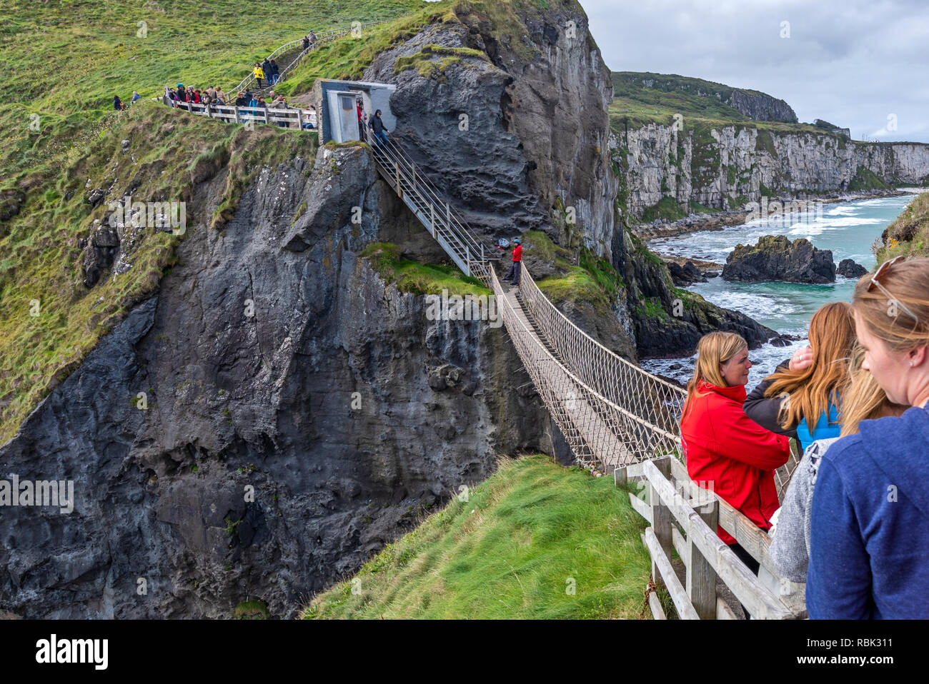 Turistas y visitantes explorar y cruzar el puente de cuerdas de Carrick-A-Rede y Larrybane Bay, en la costa oeste de Irlanda. Foto de stock