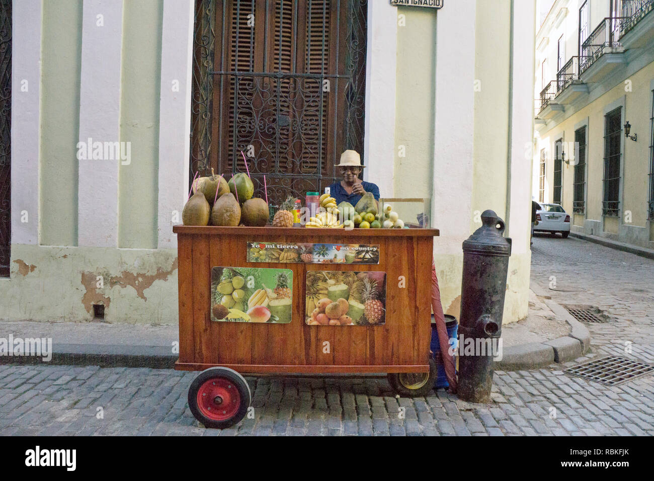 Thumbs up de proveedor de frutas cubanas detrás de su alegre carro de madera apiladas con cocos ya perforados con pajas, así como otras frutas Foto de stock
