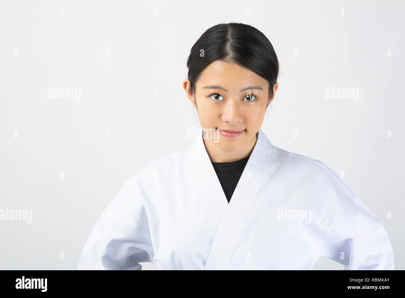 Hermosa joven mujer vistiendo traje de karate poniendo las manos en las caderas sobre fondo blanco. Foto de stock