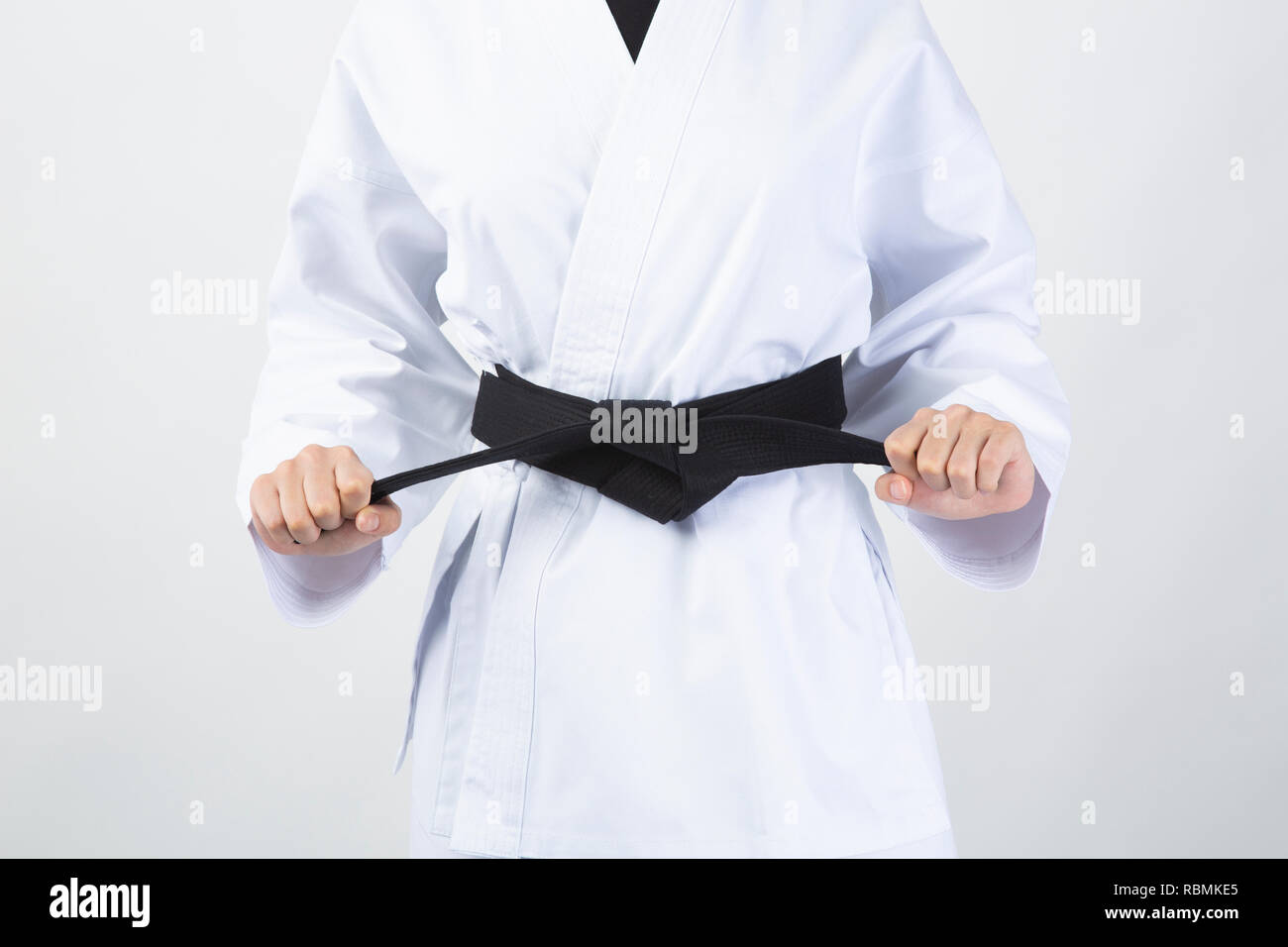 Cinturón Negro celebrada por mujer vistiendo traje de karate sobre fondo blanco. Foto de stock