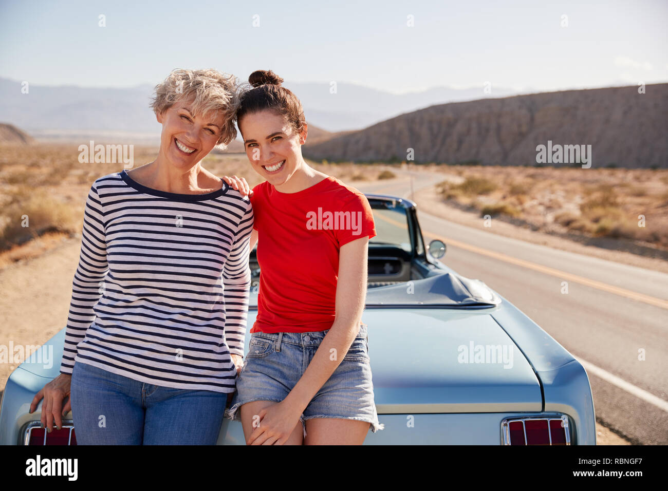 Madre e hija adulta en viaje por carretera inclinada contra el coche Foto de stock
