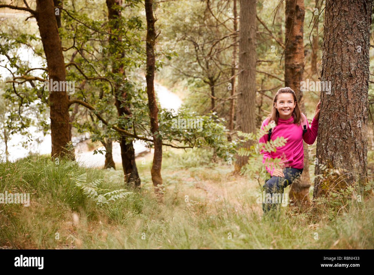 Pre-teen girl está apoyado contra un árbol en un bosque, visto a través de la hierba alta Foto de stock
