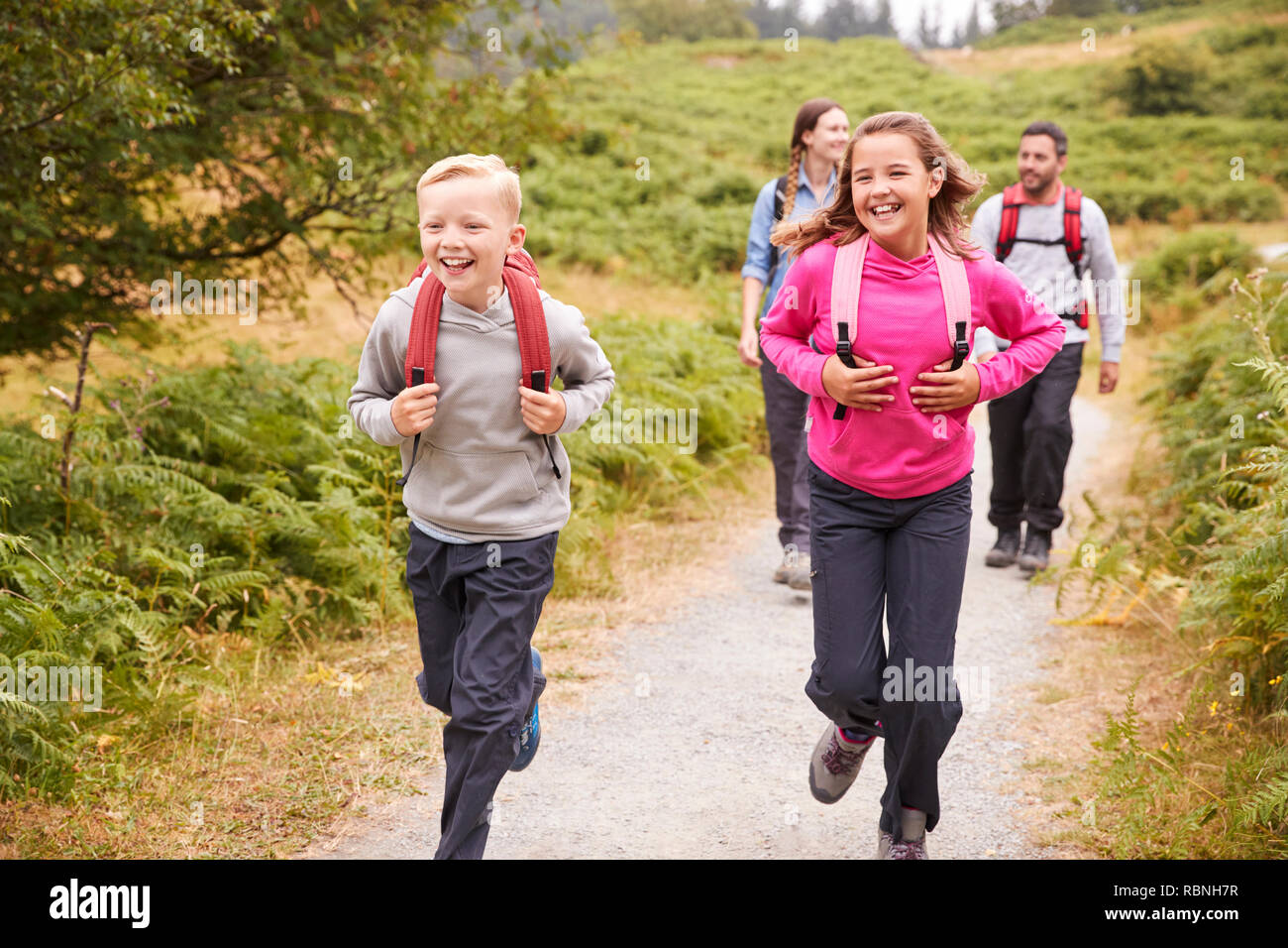 Cerca de los niños corriendo delante de los padres en un país camino durante unas vacaciones en familia, vista frontal Foto de stock