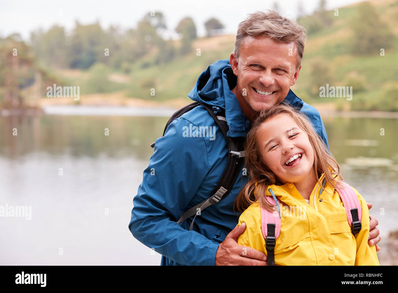 Pre-adolescentes caucásicos chica de pie con su padre en la orilla de un lago, reírse de la cámara, cierre arriba Foto de stock