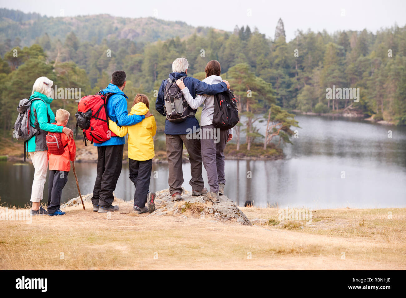 Familia de generación múltiple abrazar y admirar las vistas al lago, vista posterior, Lake District, RU Foto de stock