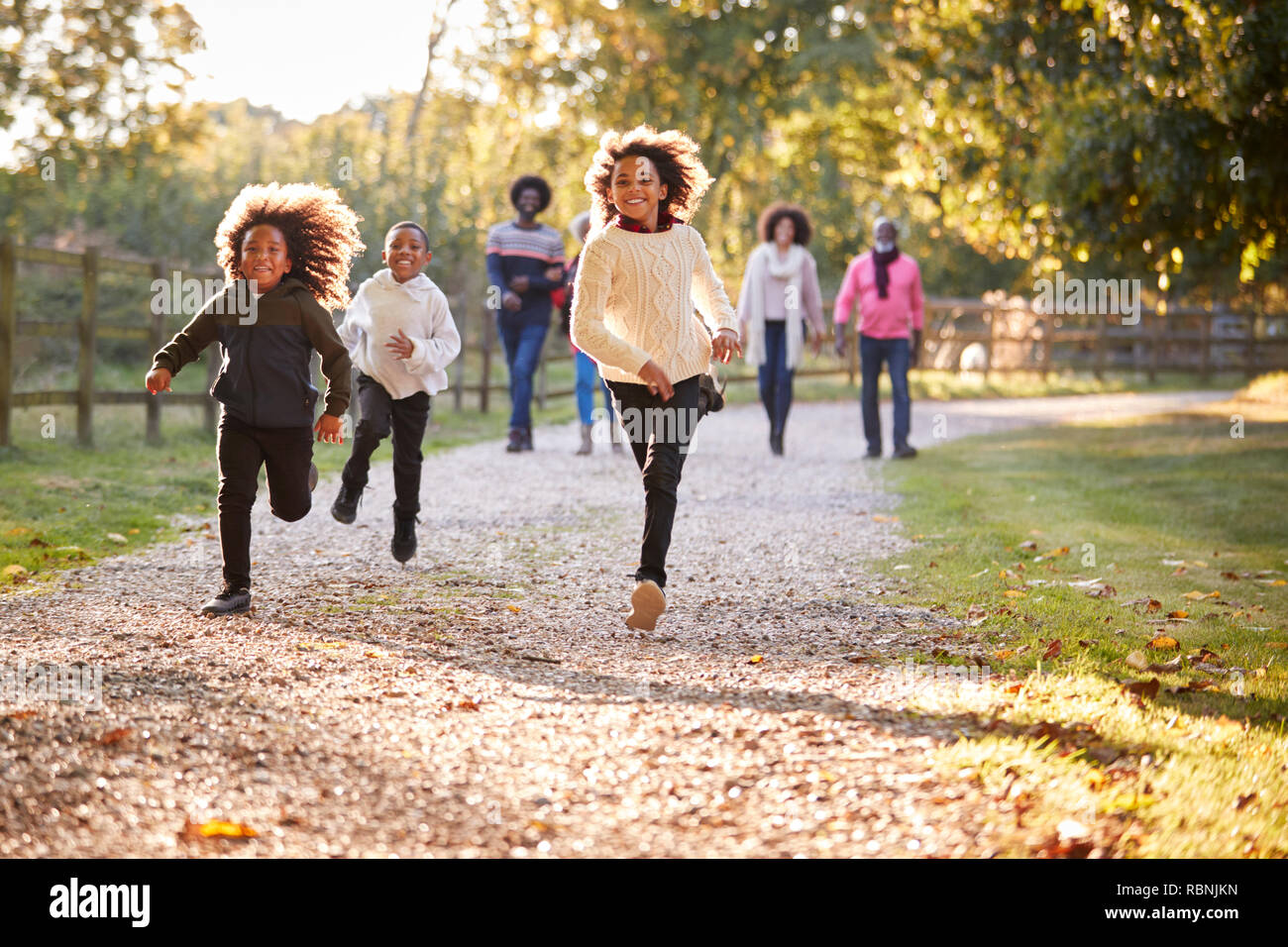 Los niños corriendo delante como Multi generación familiar disfrute de otoño a pie de campo juntos Foto de stock