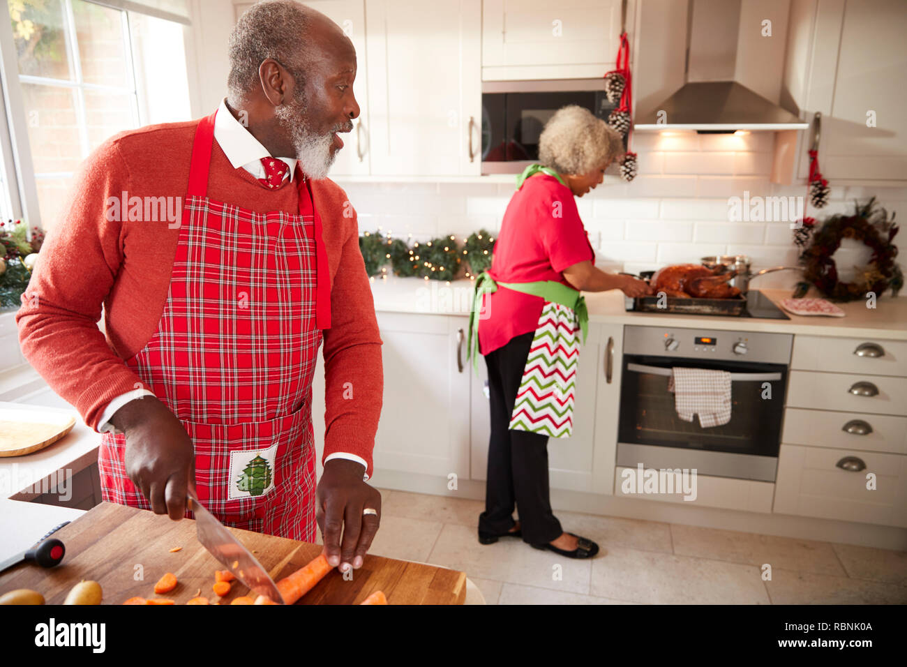 Maduras negras par preparar la cena de Navidad, hombre cortando verduras en primer plano, pasando a su compañero, que está preparando el pavo Foto de stock