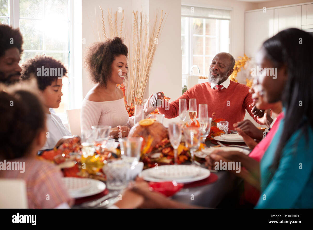Varias generaciones de la familia de raza mixta manos y diciendo la gracia antes de comer en la mesa de la cena de Acción de Gracias, el enfoque selectivo Foto de stock