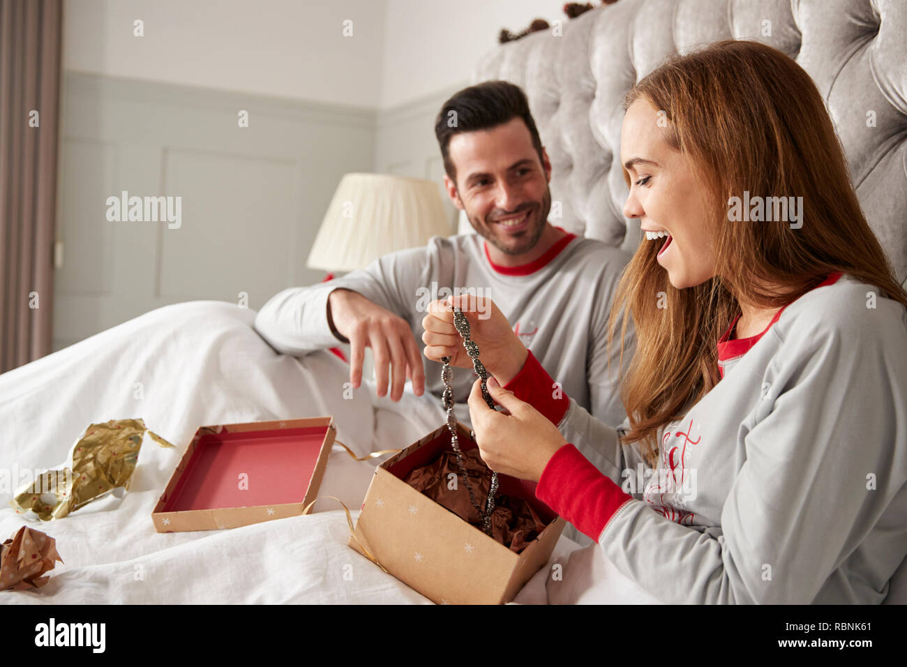 Mujer Apertura de Regalo Collar en la cama en casa como cambio de pareja se presenta en el día de Navidad. Foto de stock