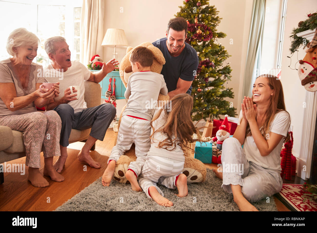 Niños jugando con Oso de peluche gigante como familia Multi-Generation abrir los regalos el Día de Navidad Foto de stock