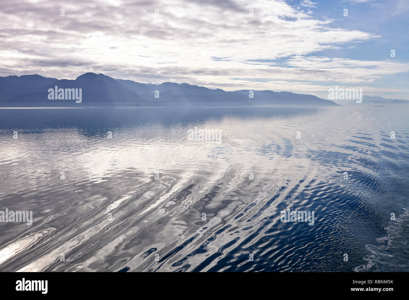 Estela de barco en el lago en Alaska, rodeado por montañas y bosques Foto de stock
