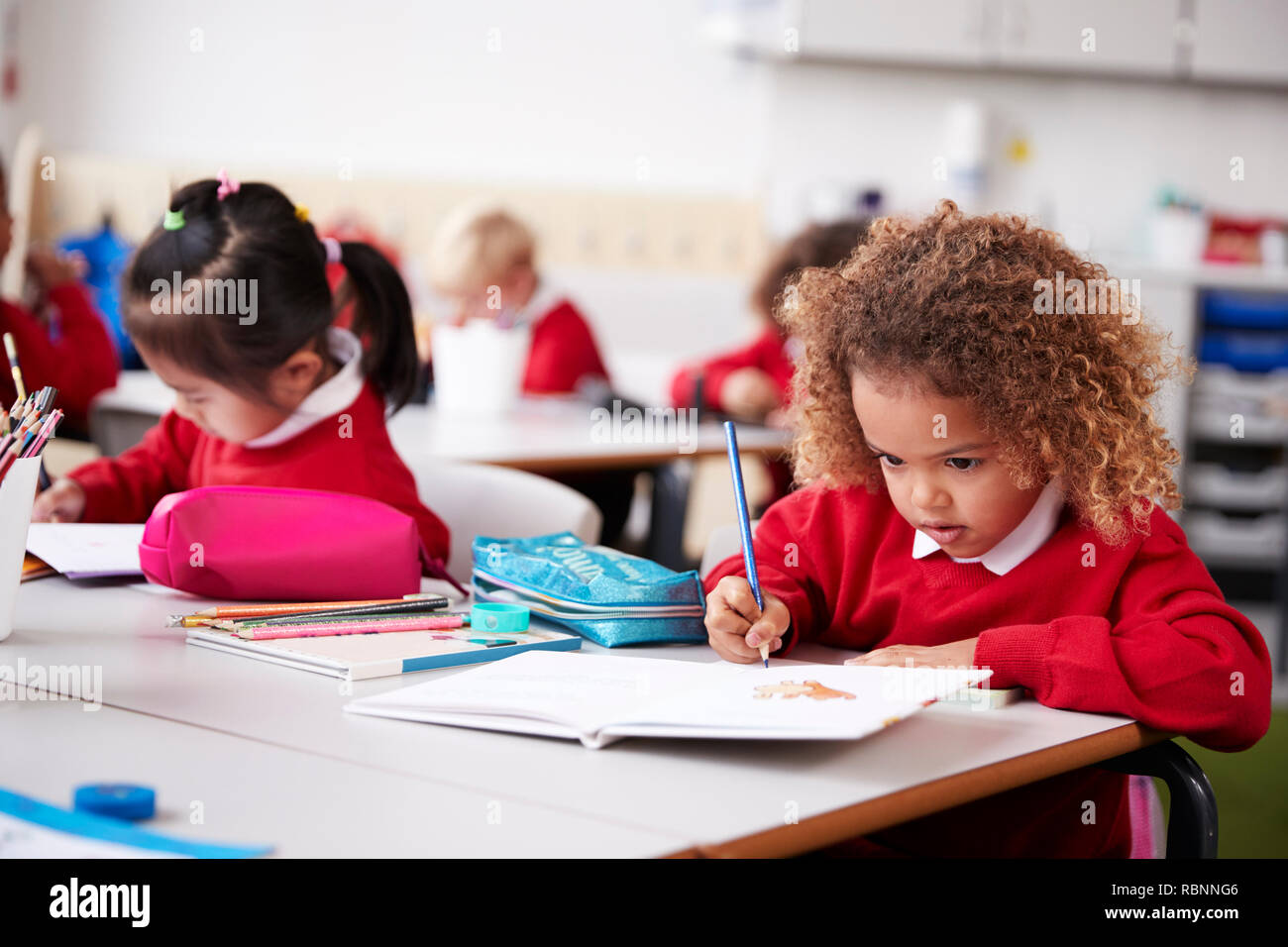 Colegiala vistiendo uniforme escolar sentado en una mesa en un aula de la escuela infantil de dibujo, cerrar Foto de stock