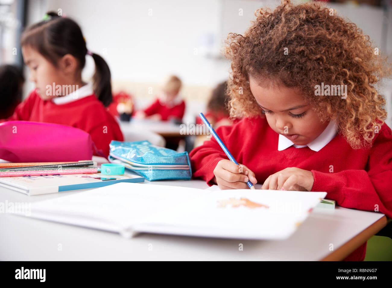 Alumna de raza mixta vistiendo uniforme escolar sentado en una mesa en un aula de la escuela infantil de dibujo, cerrar Foto de stock