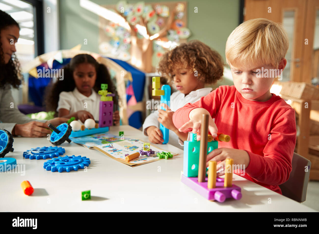 Escuela infantil muchacho sentado en una mesa con la fabricación de juguetes educativos con sus compañeros, cerrar Foto de stock