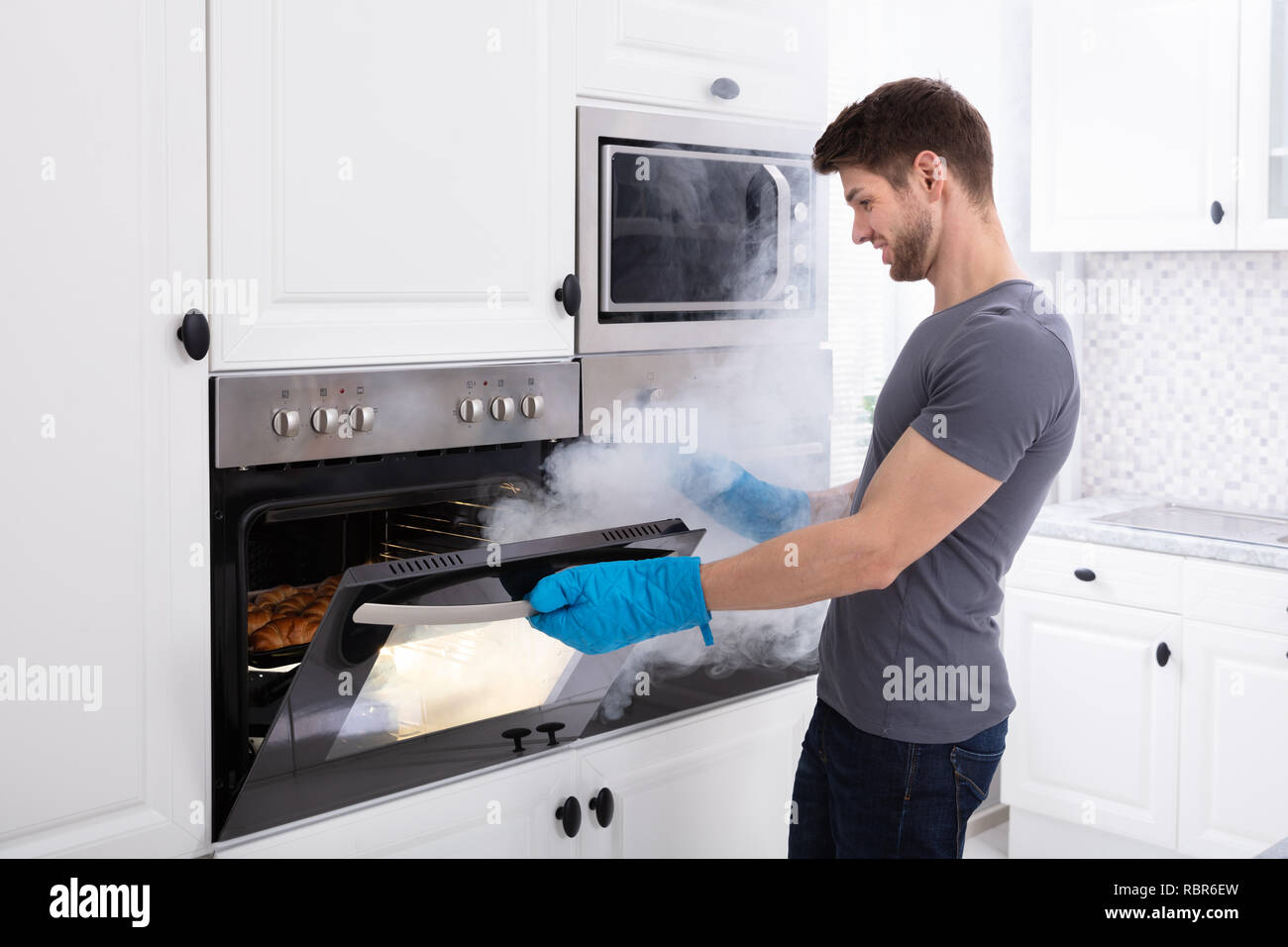 Joven con guantes, abrir el horno lleno de humo en la cocina Fotografía de  stock - Alamy