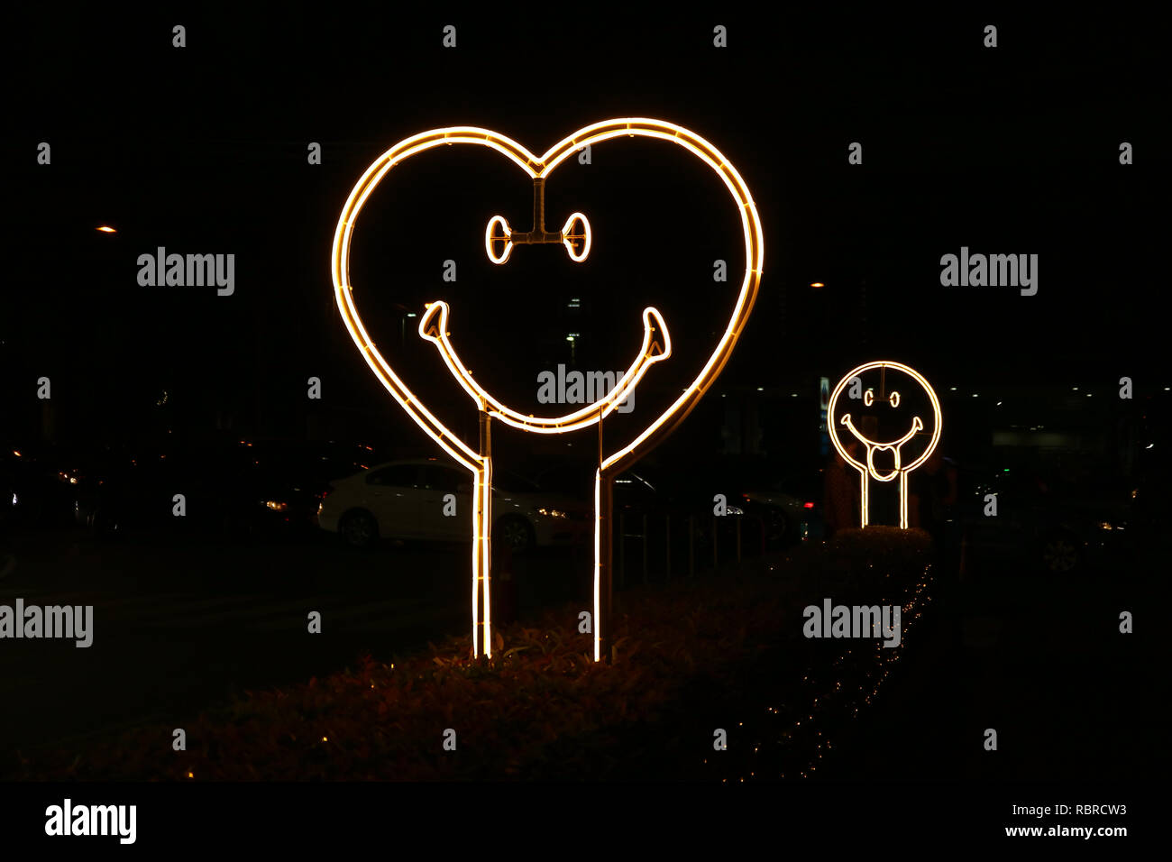 Cara sonriente en forma de corazón luz de neón signo en el lado de la calle en la noche Foto de stock