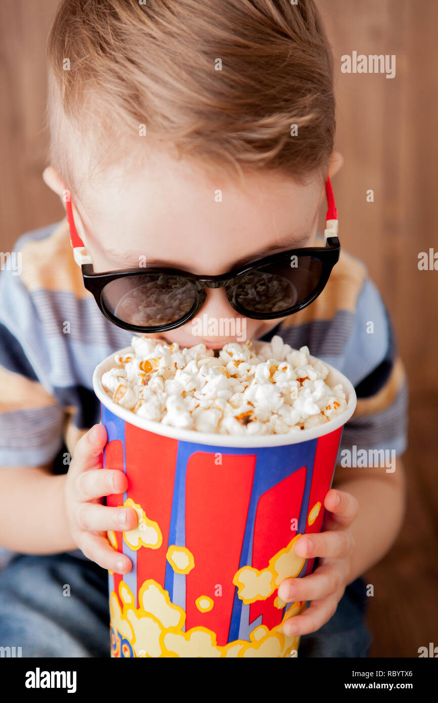 Poco chico lindo bebé niño 2-3 años , 3D IMAX cinema gafas sosteniendo la  cuchara para palomitas, comer comida rápida sobre fondo de madera. La vida  infantil para niños Fotografía de stock - Alamy
