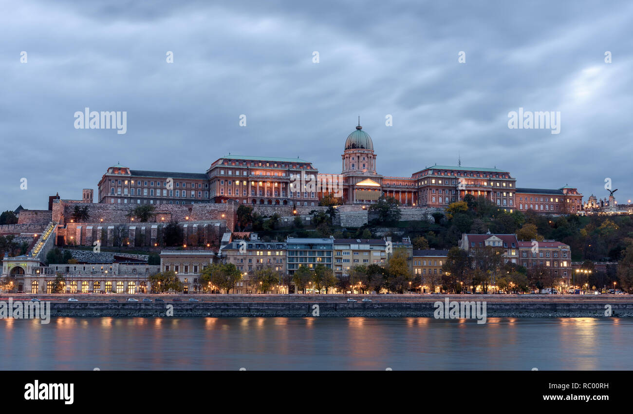 Castillo de Buda, con vistas al río Danubio, en Budapest. Es temprano en la noche, y el castillo está iluminado con luces, reflexionando sobre el río Foto de stock