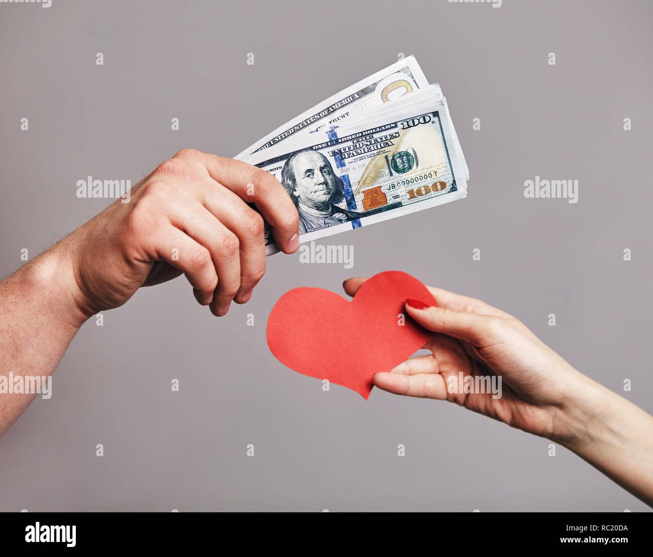 Un hombre mano sosteniendo un paquete de dinero intentando comprar un Corazones rojos de mano femenina - Compra de amor concepto Foto de stock