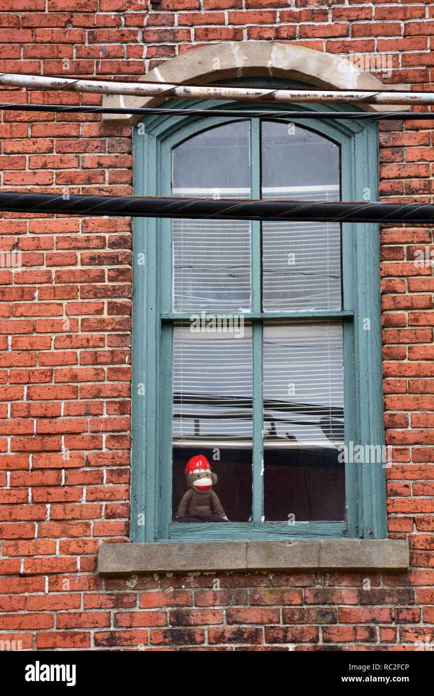 Un mono de peluche parecido a Jorge El Curioso mira por la ventana de un viejo edificio de apartamentos. Foto de stock