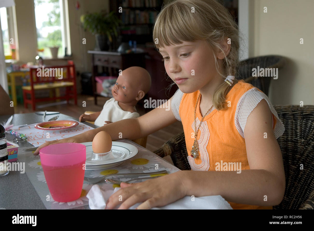 Chica joven esperando en la mesa de desayuno Wirh muñeca Foto de stock