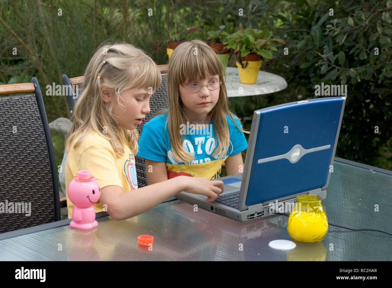 Dos mujeres jóvenes niños en los 2000s, jugando con un ordenador portátil en el jardín en verano. Foto de stock