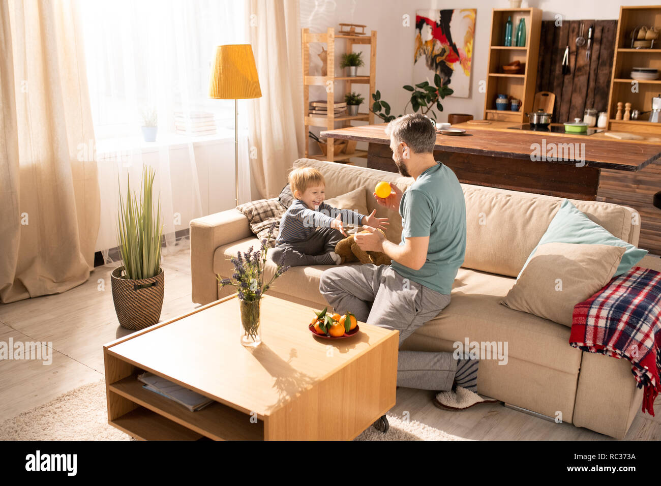 Feliz padre joven sentado en un cómodo sofá en el apartamento y jugar con  gozosa pequeño hijo, dando al muchacho de bolas de juguete Fotografía de  stock - Alamy